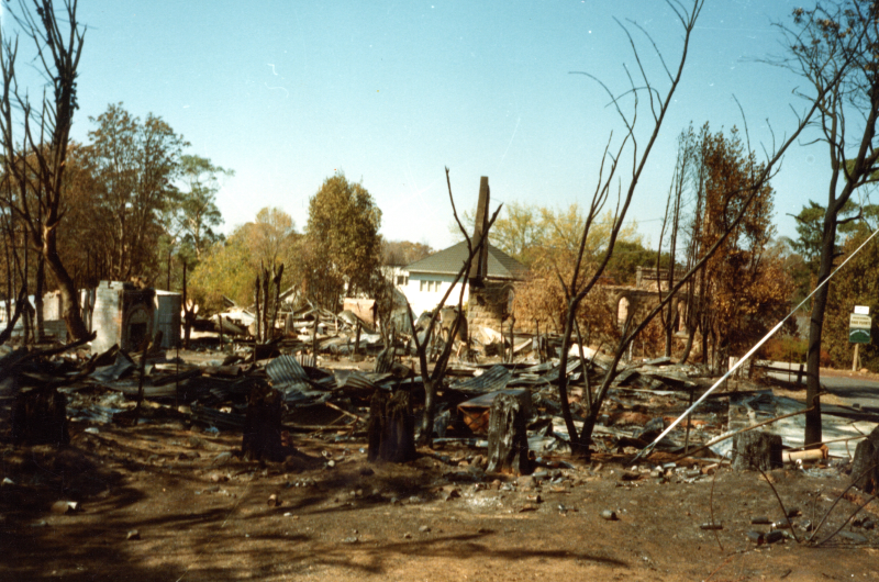 A fire-damaged house sits abandoned in a barren field, illustrating the aftermath of devastating wildfires.