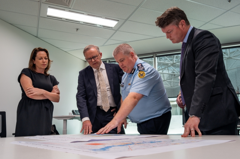 Four people examine a map on a table, with Anthony Albanese leaning in as Tim Wiebusch points to a location